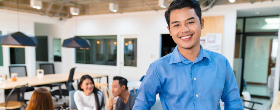 Happy man and three coworkers in the background at the Seguros Confie lunch room.