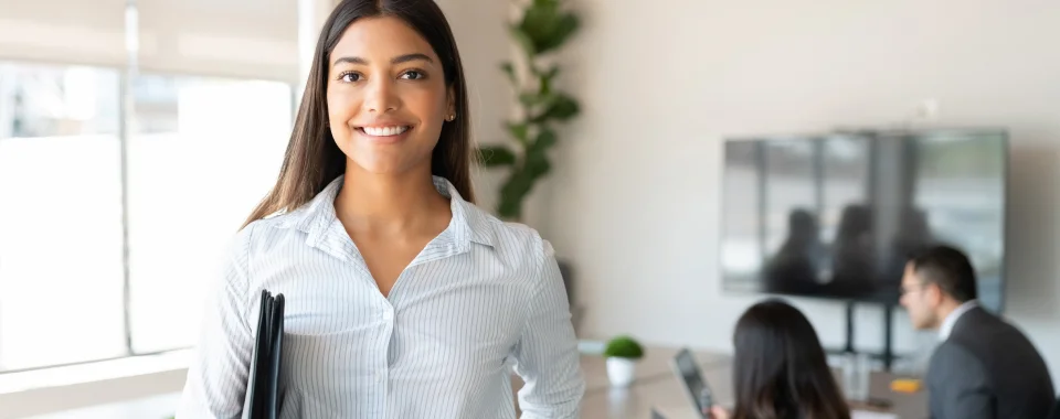 Happy woman and two coworkers in the background at the Seguros Confie meeting room.