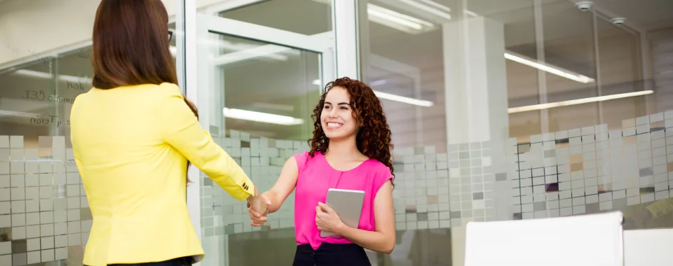 Two women shaking hands at the Seguros Confie meeting room.