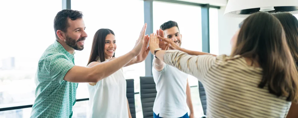 A group of two men and three women joyining hands at the center of a circle at the Seguros Confie meeting room.