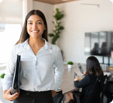 Happy woman and two coworkers in the background at the Seguros Confie meeting room.