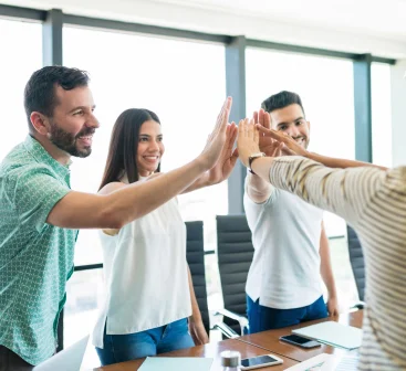 A group of two men and three women joyining hands at the center of a circle at the Seguros Confie meeting room.