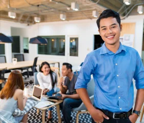Happy man and three coworkers in the background at the Seguros Confie lunch room.