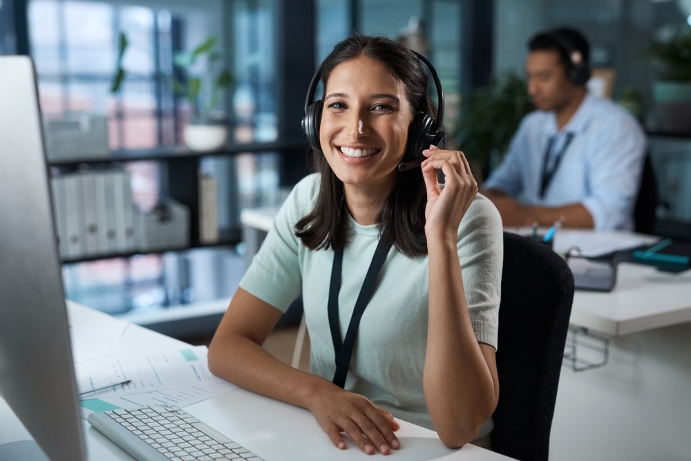 Portrait of a young woman using a headset and computer in a modern office.