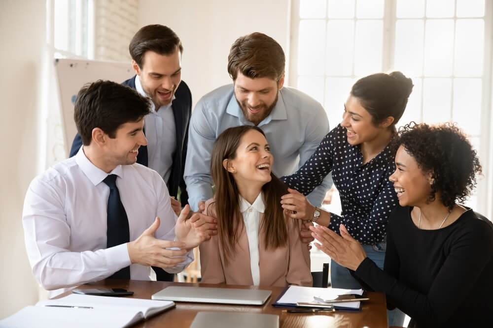 Diverse team celebrating a coworker’s success during a business meeting, representing career growth and professional development opportunities.