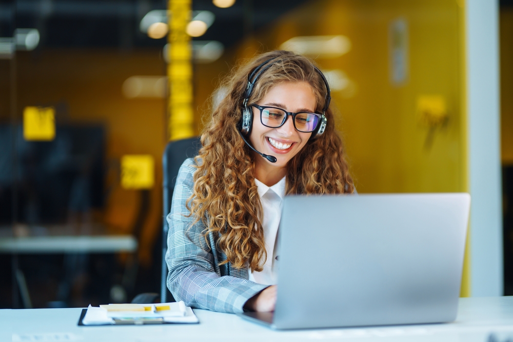 female customer service agent on laptop with head set on smiling