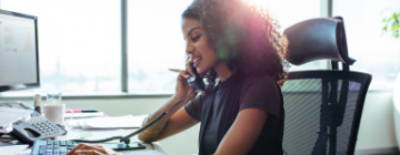 woman on phone in front of computer in her office