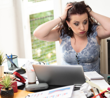 Frustrated female employee sits at cluttered workspace