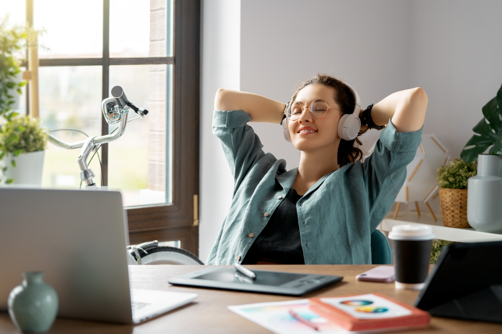 Young woman sits behind neat desk with headphones on