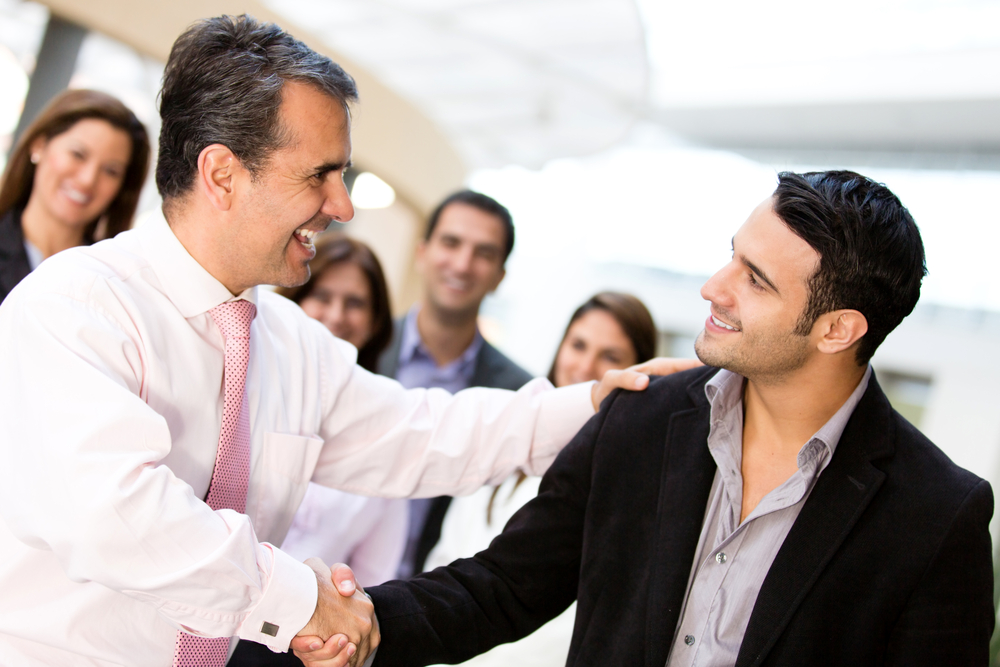 A manager shakes hands and congratulates an employee