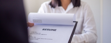 Interviewer's hand holds resume while job applicant looks on across the desk