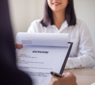Interviewer's hand holds resume while job applicant looks on across the desk