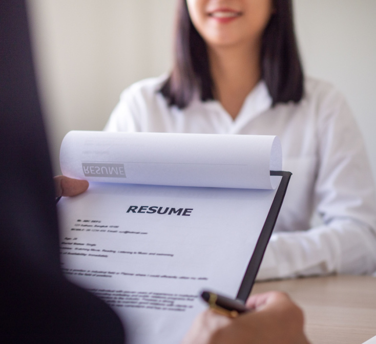 Interviewer's hand holds resume while job applicant looks on across the desk