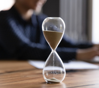 Image of an hourglass on a desk with a person in the background working