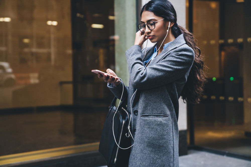 Ethnic woman walks to work and checks her fitness app