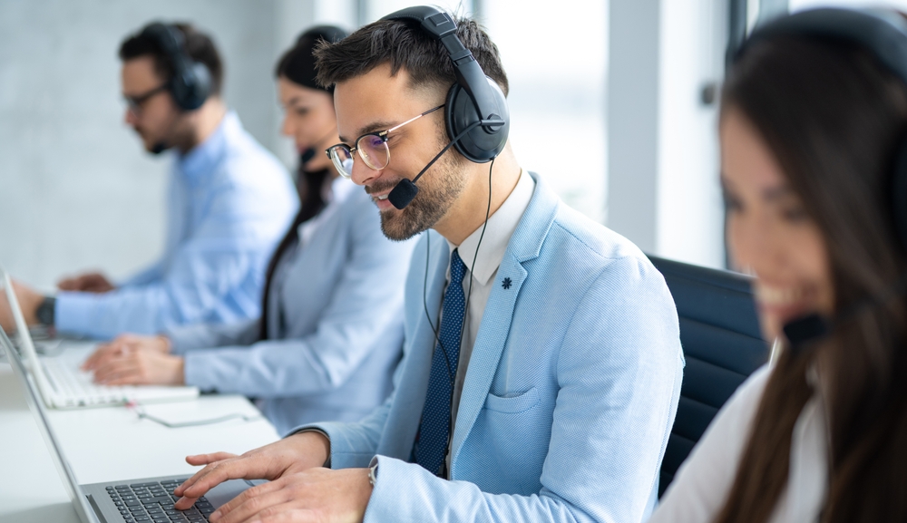 Young man on headset smiling as he talks to customer