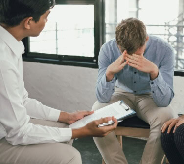 Man sitting with head in hands while two colleagues talk with him, demonstrating conflict resolution skills in a workplace discussion.