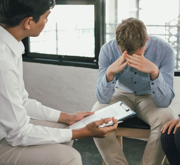 Man sitting with head in hands while two colleagues talk with him, demonstrating conflict resolution skills in a workplace discussion.