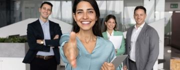 Woman reaches out for a handshake with a hiring team behind her, creating a welcoming moment for people looking to find work in Mexico.