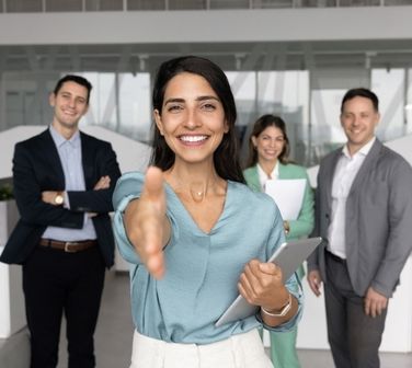 Woman reaches out for a handshake with a hiring team behind her, creating a welcoming moment for people looking to find work in Mexico.