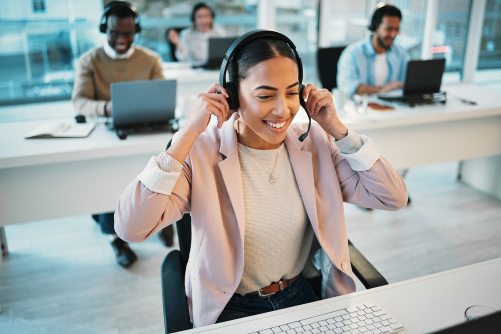 Young professional Hispanic woman smiles as she puts on her headphones in a call center - customer service jobs in Mexico