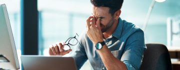 Man sitting at computer rubbing his eyes from eye strain