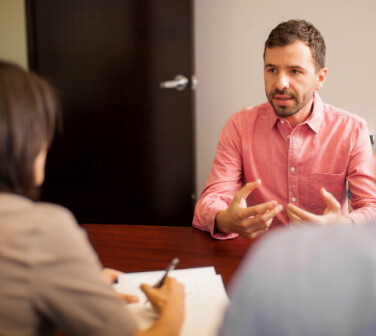 A young man facing the camera interviews for a sales representative job in a call center with two company representatives whose backs are to the camera, best jobs in Tijuana.