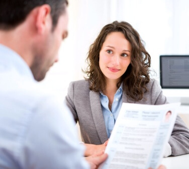 Call center hiring manager looks over resume from woman applying for call center job in Tijuana, sitting across the desk.