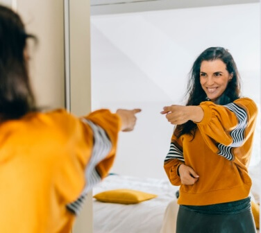 Employee smiling at their reflection in a mirror to reinforce positive self talk at work and build confidence.