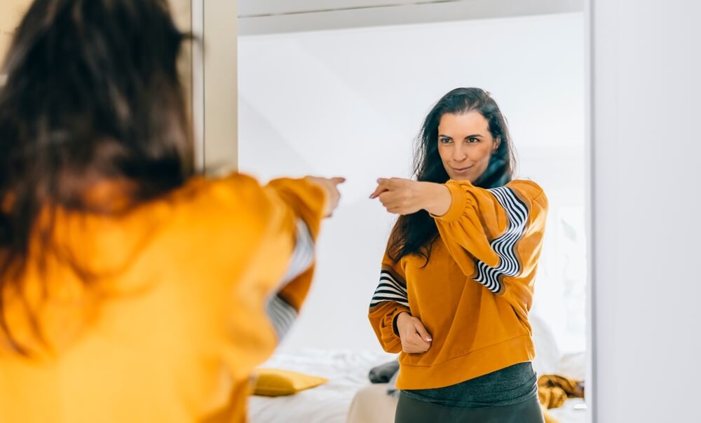 Woman pointing at herself in the mirror, concept of positive self talk.