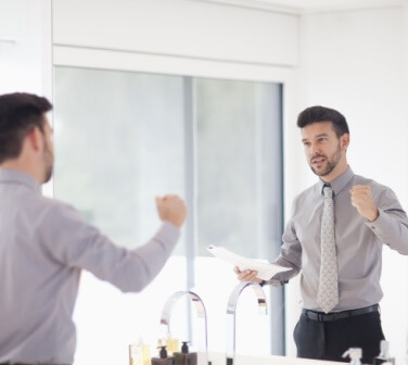 A young man looking in the mirror and giving himself a pep talk, positive self talk.