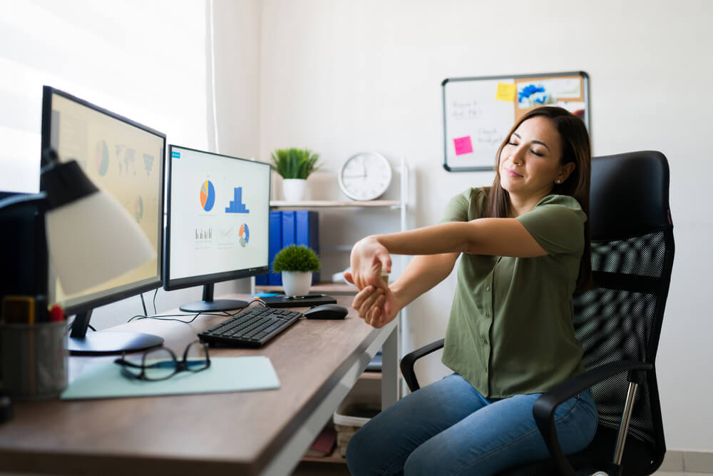 A woman at her desk performs wrist flexing exercises to help with carpal tunnel syndrome - best call center in Tijuana.