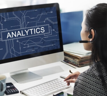 Call Center agent with headphones in front of her computer which says Analytics - Seguros Confie, Best Call Center in Tijuana.
