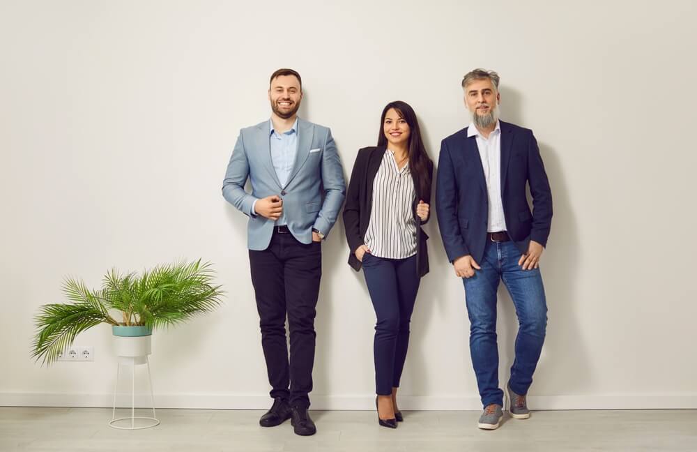 Three smiling business people wearing casual business attire.