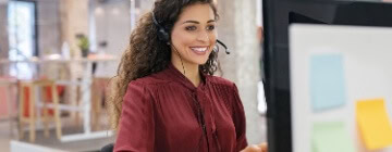 A female call center agent smiling while working, answering calls relaxed due to practicing self-motivation strategies for call center agents - Seguros Confie, the Coolest Call Center.