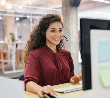 A female call center agent smiling while working, answering calls relaxed due to practicing self-motivation strategies for call center agents - Seguros Confie, the Coolest Call Center.