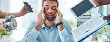 Young man has a headache as stress mounts by coworkers handing items to him - best call center job in Tijuana.