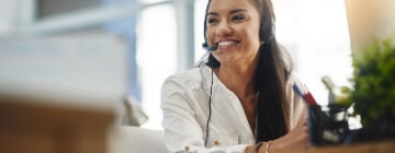 Smiling young woman looks at her computer and speaks into a headset - best call center jobs in Tijuana.