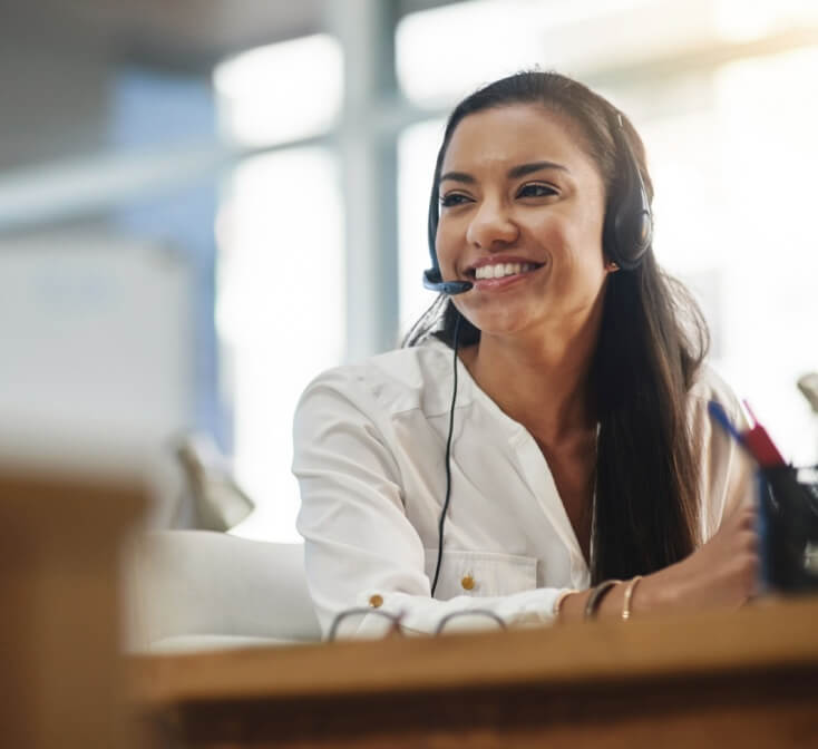 Smiling young woman looks at her computer and speaks into a headset - best call center jobs in Tijuana.