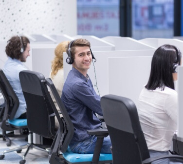 Male call center agent sitting in row of agents working in cubicles turns and smiles at camera - best call center jobs in Tijuana.