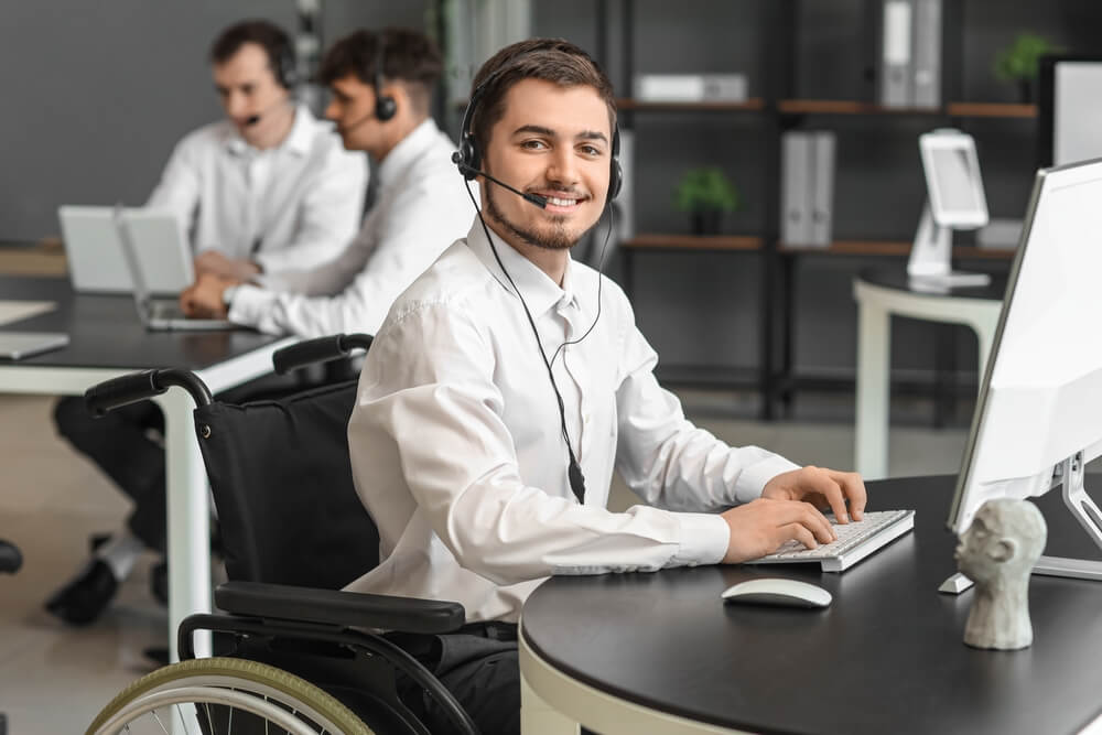 Smiling male call center agent in a wheelchair working with customers on his laptop - best call center jobs in Tijuana.