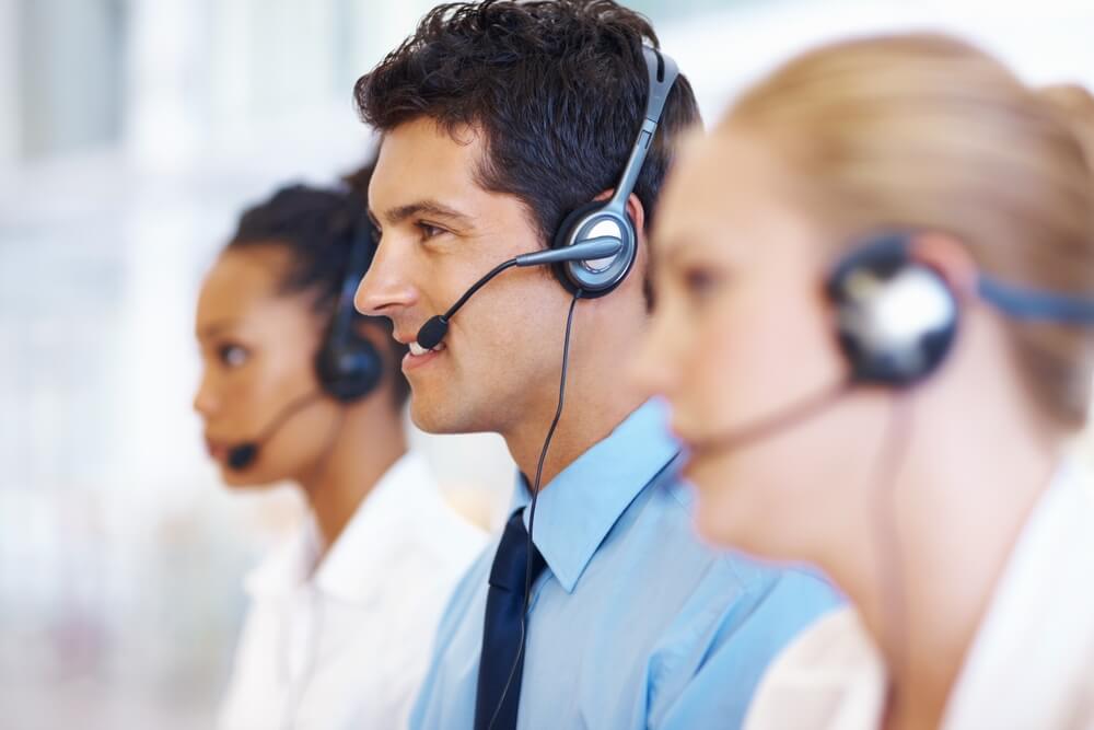 Three call center agents in a row with the man in the middle in focus and smiling, bilingual call center agent - best call center in Tijuana.