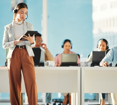 Professional businesswoman leading and supervising a group of Call Center employees, providing guidance and generating reports at office.