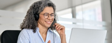 Happy mature business woman call center representative customer support agent talking to client, smiling middle aged senior female operator wearing headset working using laptop computer in office.