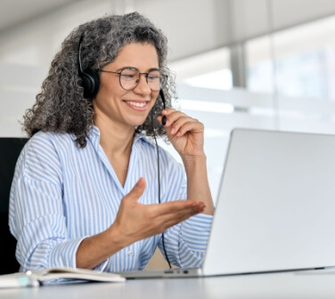 Happy mature business woman call center representative customer support agent talking to client, smiling middle aged senior female operator wearing headset working using laptop computer in office.