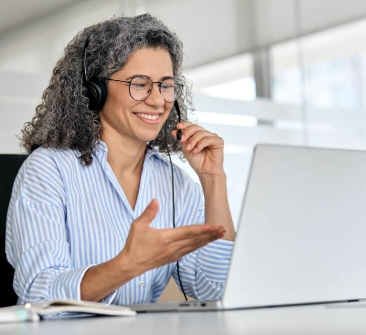 Happy mature business woman call center representative customer support agent talking to client, smiling middle aged senior female operator wearing headset working using laptop computer in office.