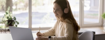 Girl wearing headphones using laptop in call center, improve foreign language skills, gain new knowledge online.