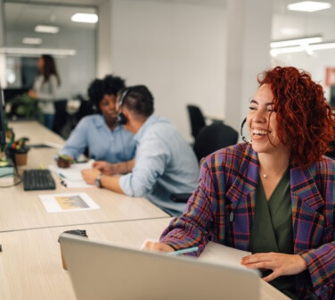 Smiling customer services agent woman with headset working in an office. Portrait of a female agent working on a laptop in a call center and talking with clients and customers.