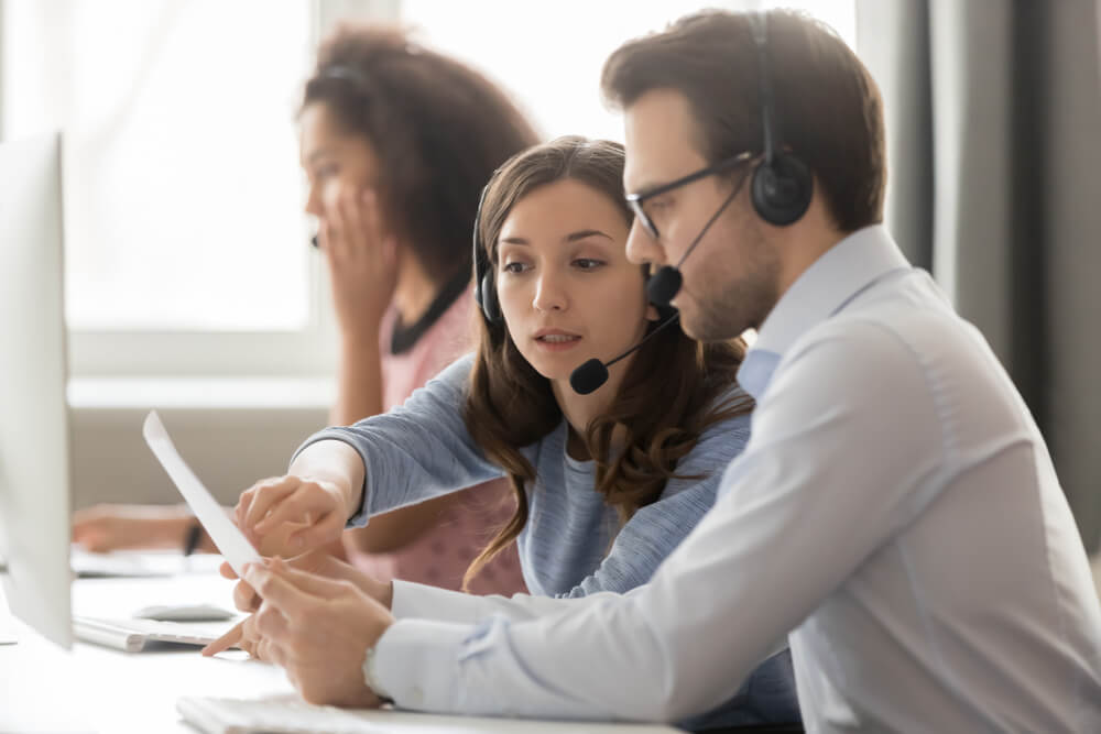 Call center service agents operators in wireless headsets helping in teamwork at workplace, learning time management skills in busy call center.