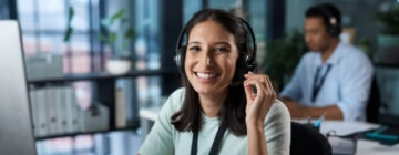 Young professional woman smiling while working in a modern office call center, representing financial independence for young professionals.